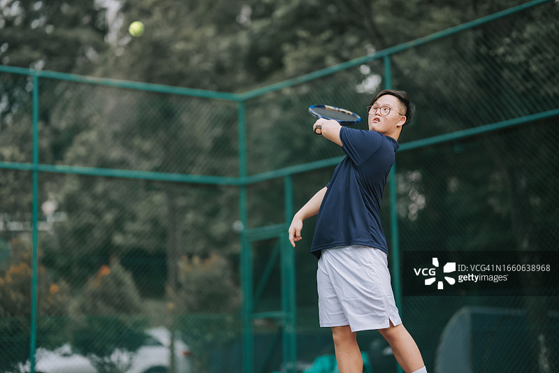 患有唐氏综合症的亚洲华人年轻人在网球场学习网球图片素材