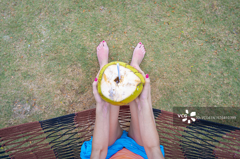 吊床上喝新鲜椰子水的女子俯视图图片素材