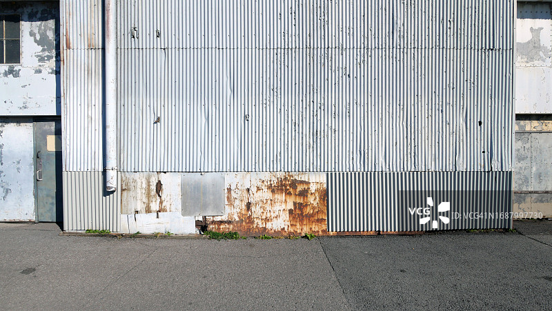 加拿大魁北克省蒙特利尔，用波纹金属板制成的风化墙，涂上灰色的油漆和油漆，门和沥青街道图片素材