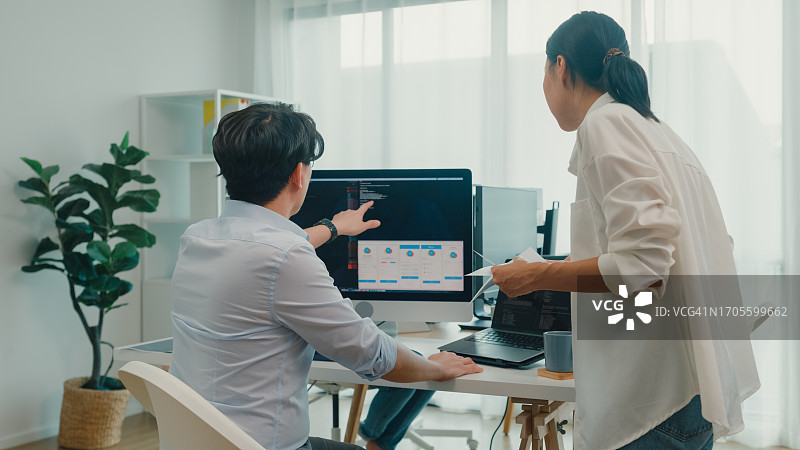 一群亚洲人，软件开发人员坐在办公桌前用电脑写代码，办公室里有多个屏幕。程序员开发。图片素材