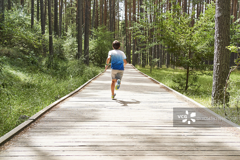 一个穿着休闲服的旅游男孩的后视图，在森林中央修建的一条木道上奔跑图片素材