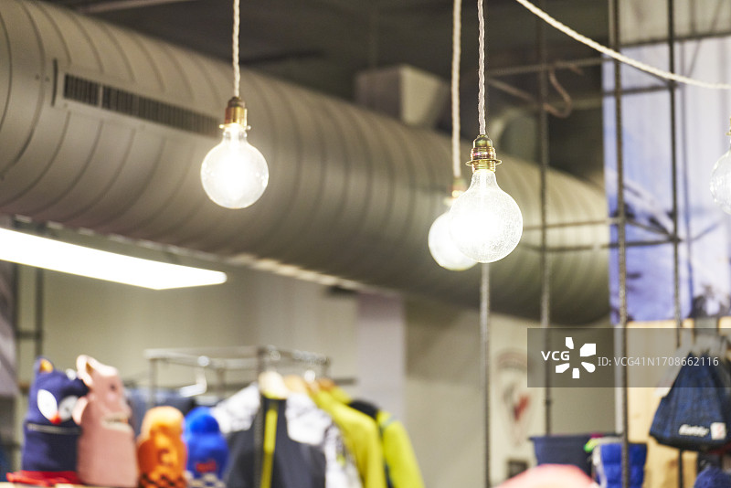 一组灯泡悬挂在一家服装店的天花板上，周围没有人，侧视图图片素材