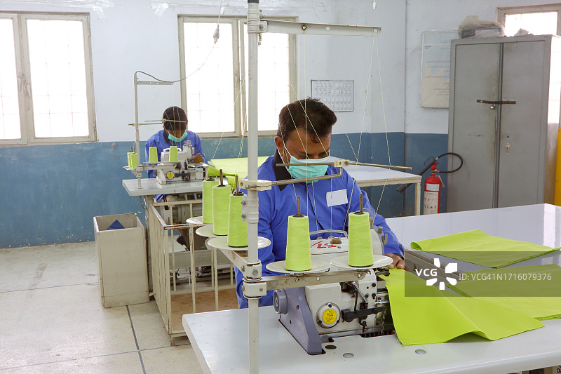 两名男工人在一家纺织厂的缝纫部用电动缝纫机缝制布料。图片素材