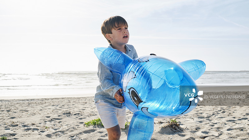 阳光明媚的一天，一个男孩在海滩上玩着充气鲨鱼玩具图片素材