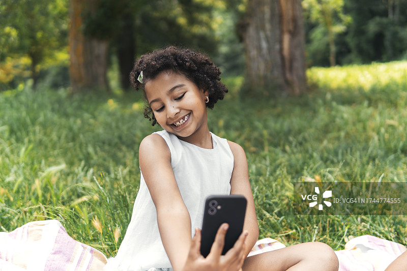 微笑的女孩在花园里用智能手机自拍图片素材