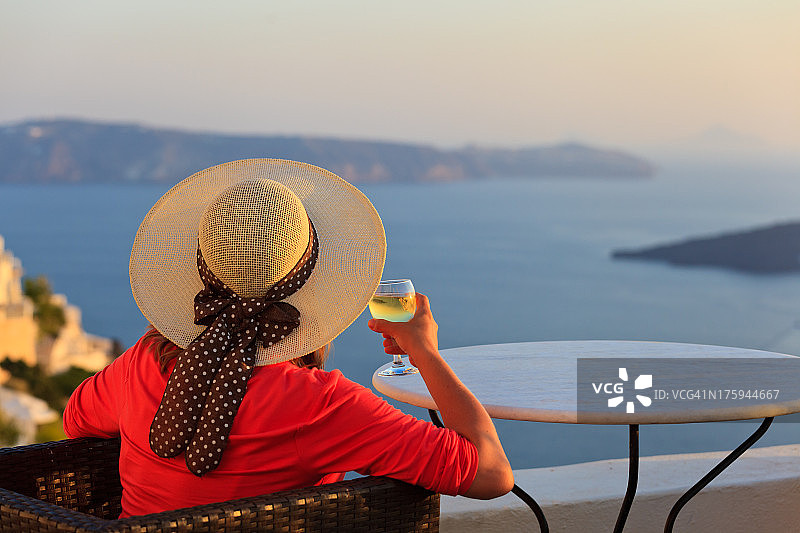 在希腊圣托里尼，一个女人喝着葡萄酒欣赏日落图片素材
