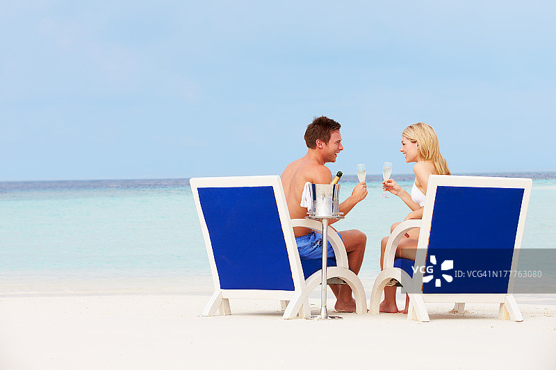 一对情侣在沙滩上坐在椅子上放松，喝着香槟图片素材