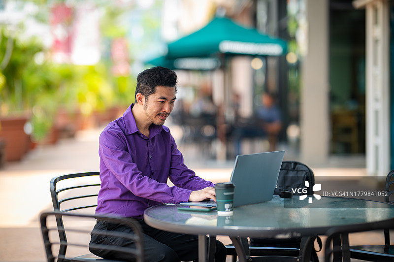 一名亚裔中国商人在路边咖啡馆远程办公时用笔记本电脑上网图片素材