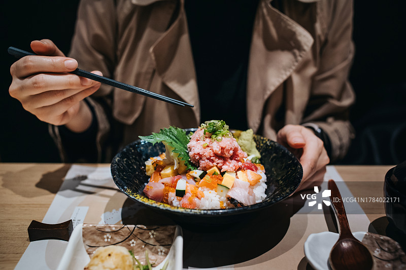 特写，年轻的亚洲妇女在享用新鲜的生鱼片米饭，在一家日本餐馆里。亚洲美食和饮食文化。美食家。体验式旅行和度假。人，食物和生活方式图片素材