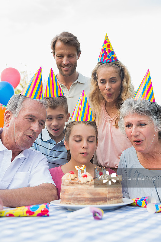 欢乐的一家人看着女孩在生日聚会上吹蜡烛图片素材