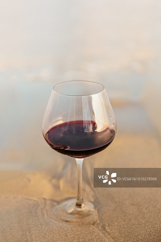 日落时，海边沙滩上的一大杯红酒的特写图片素材