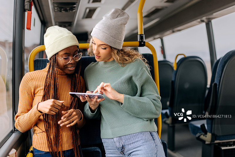 年轻的女性朋友在一起乘公共汽车时玩手机图片素材