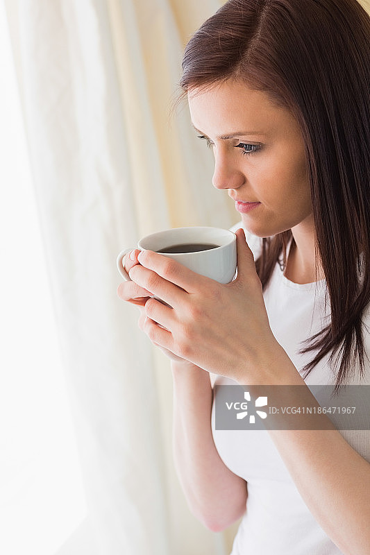 沉思的女孩拿着一杯咖啡，看着别处图片素材