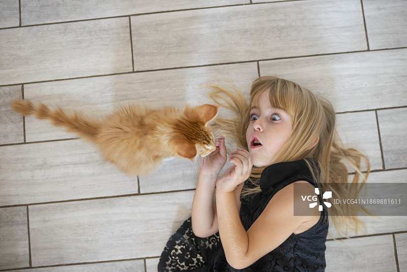 可爱的女孩躺在地板上和小猫在家里玩图片素材