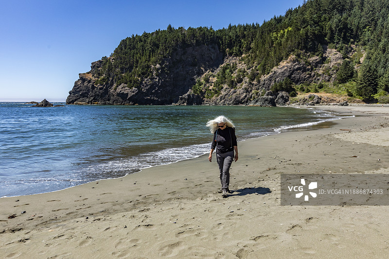 美国，俄勒冈州，布鲁金斯，阳光明媚的一天，一位老年妇女在海滩上散步图片素材