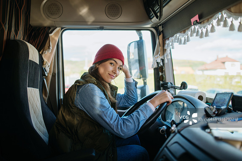 一名女性职业卡车司机坐在一辆大卡车上，看着镜头，微笑着。车内。女司机的概念，长途卡车运输。图片素材