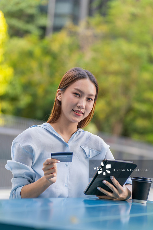 一名亚洲妇女在户外公园用数字平板电脑进行数字银行信用卡交易，桌上放着一杯咖啡图片素材