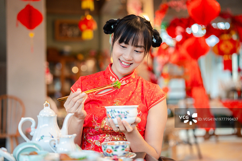 烹饪的优雅:穿着传统服饰的亚洲年轻女子品味中国美食。图片素材