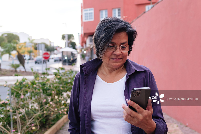 在城市街道上查看智能手机的老年妇女图片素材