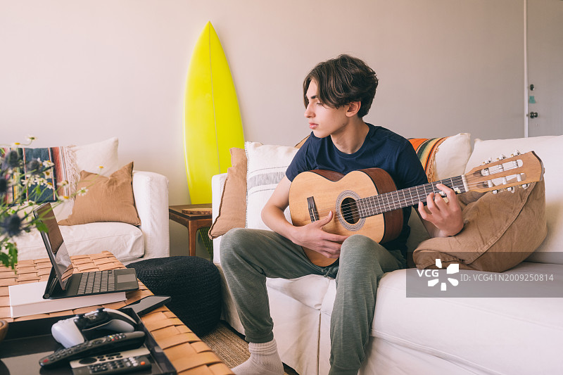 十几岁的男孩在家里的客厅里通过笔记本电脑学习吉他图片素材