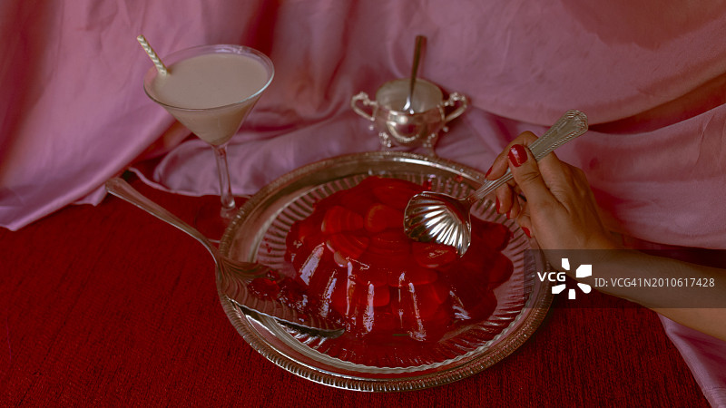红色果冻蛋糕充满心和手与勺子与牛奶鸡尾酒在粉红色的背景。情人节图片素材