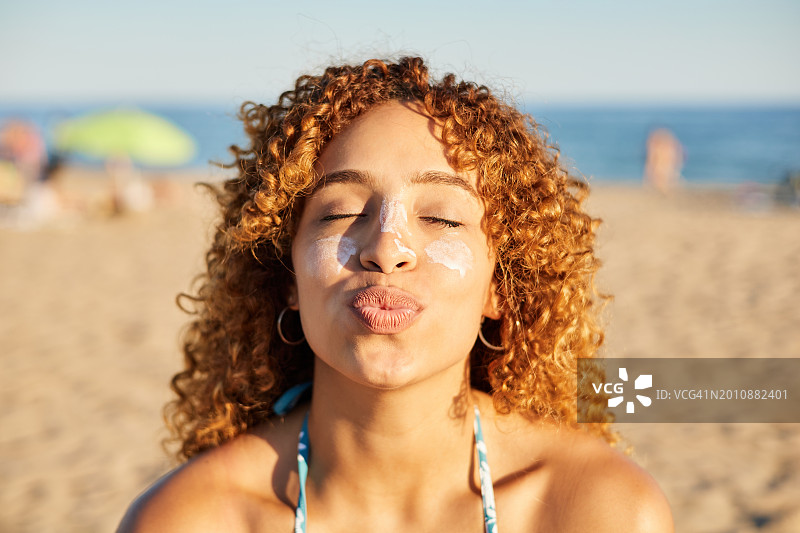 一个微笑的快乐的女人在日落的海滩上给她的脸涂防晒霜。图片素材