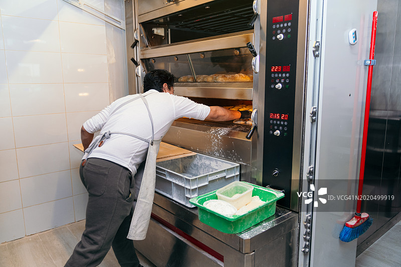 面包师在面包店的商用烤箱中检查面包质量图片素材
