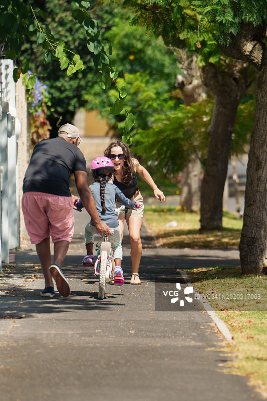 父母教他们的小女孩如何在夏天骑自行车图片素材