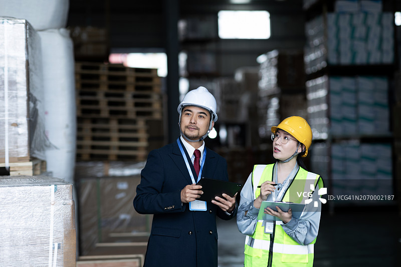 一名亚洲男性经理和一名物流工程师在平板电脑上讨论如何审计和改进仓库的运营和工作流程，以提高客户满意度。图片素材