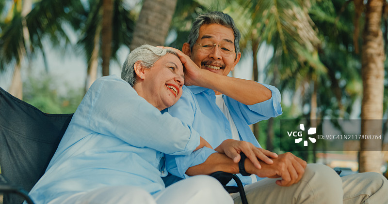 一对快乐的亚洲老夫妇坐在沙滩椅上欣赏海景，面带微笑。一个快乐的老年人享受退休后的旅行生活方式。图片素材