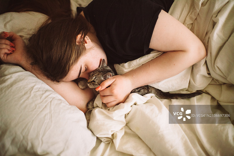快乐的年轻女子躺在床上亲吻她的小猫图片素材