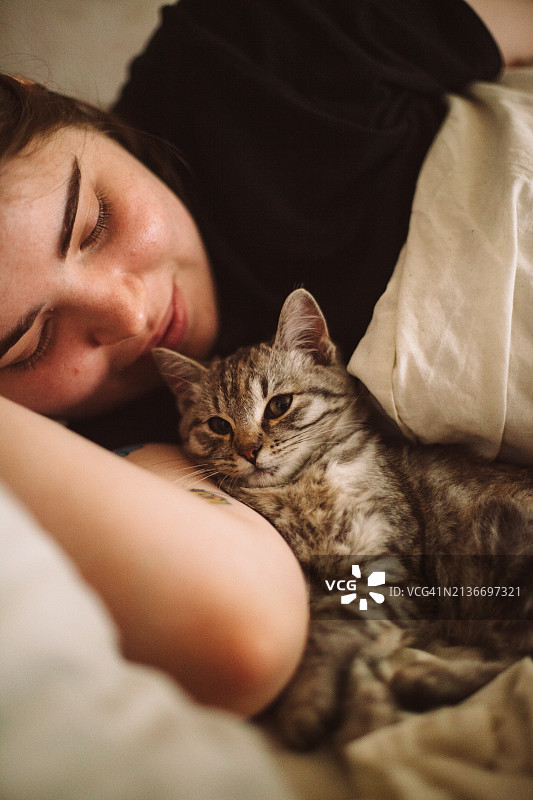 快乐的年轻女人和她的小猫躺在床上图片素材
