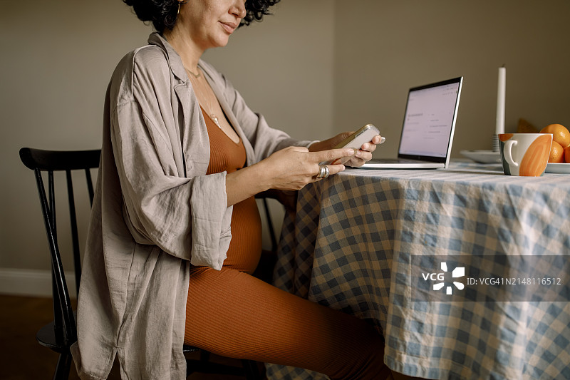 孕妇坐在家里餐桌旁的椅子上使用智能手机图片素材