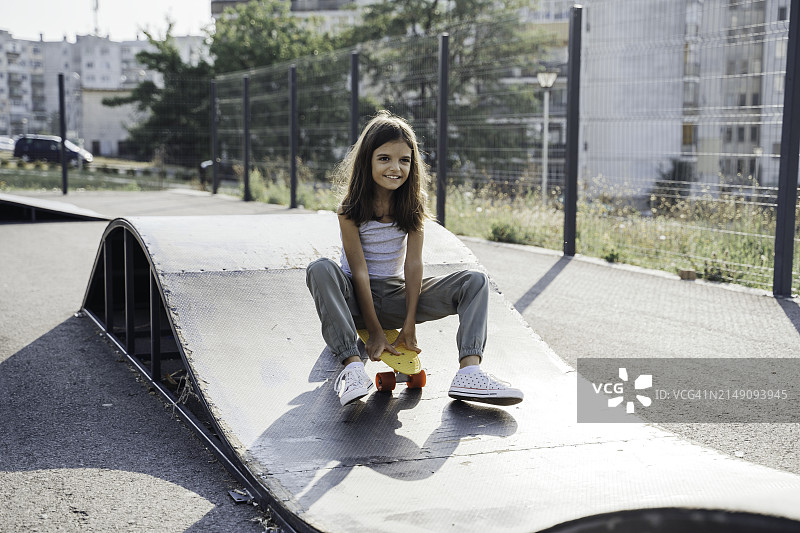 可爱的女孩正在操场上玩滑板。图片素材