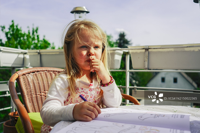 快乐的小女孩正在阳台上的桌子上用彩色铅笔画画。图片素材