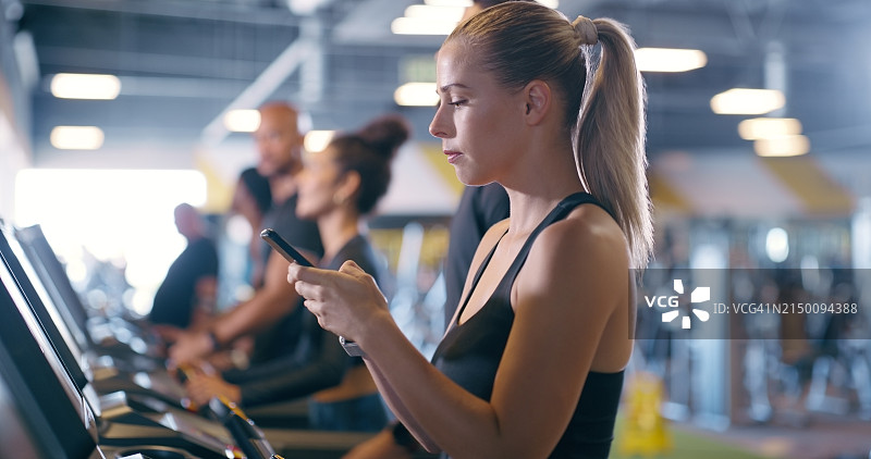 健身，应用程序和女性在健身房用手机跟踪进度，跑步机锻炼或锻炼。阅读，信息和女孩在俱乐部训练与技术监测运行结果或目标的发展图片素材