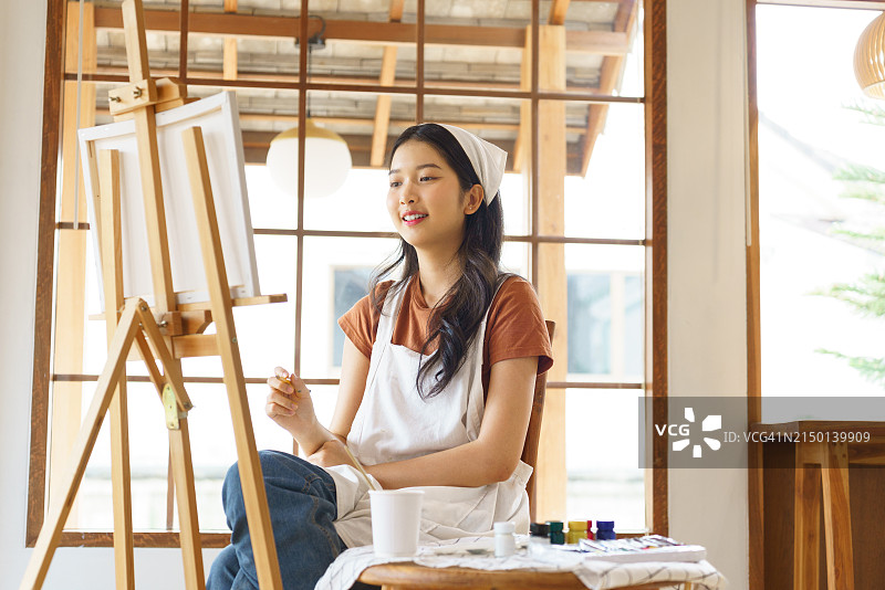 年轻的亚洲艺术家女性在工作室里以艺术爱好的生活方式创作艺术品，同时思考着设计创意杰作和在画架上绘制画布的想法图片素材