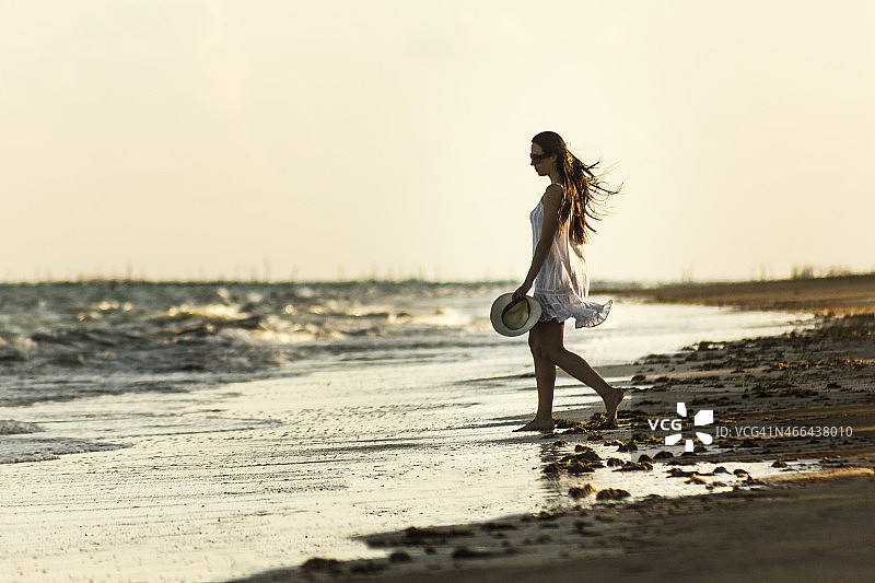 美丽的女人穿着白色漫步在荒芜的海滩图片素材