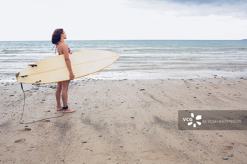 平静的女人背着冲浪板在海滩上图片素材
