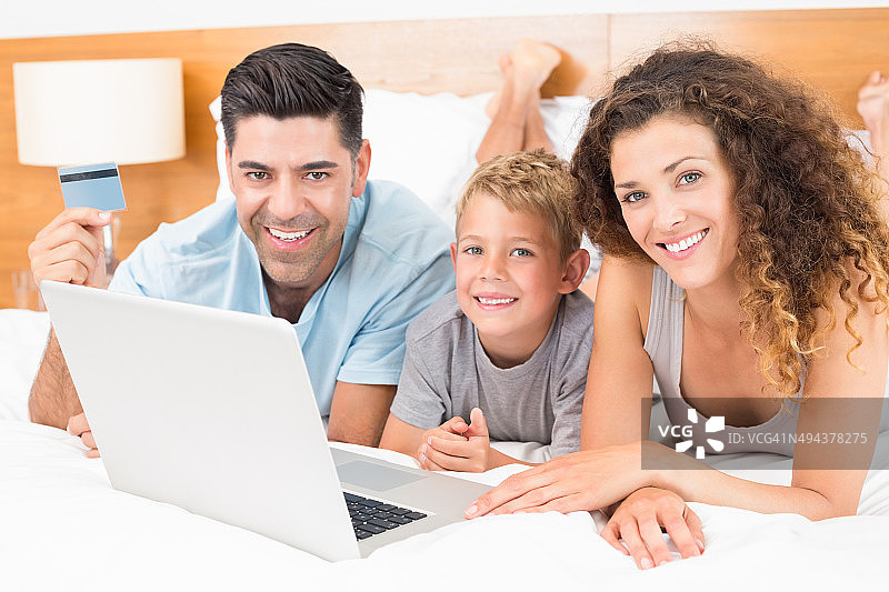 微笑的年轻家庭使用笔记本电脑在床上一起网上购物图片素材