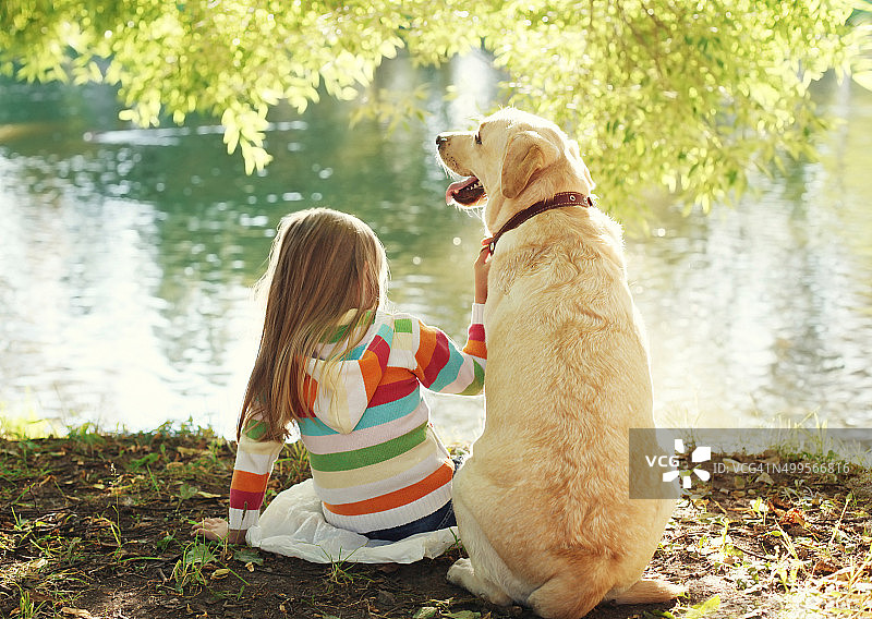 阳光明媚的夏日里，一个小孩和一只拉布拉多寻回犬坐在一起图片素材