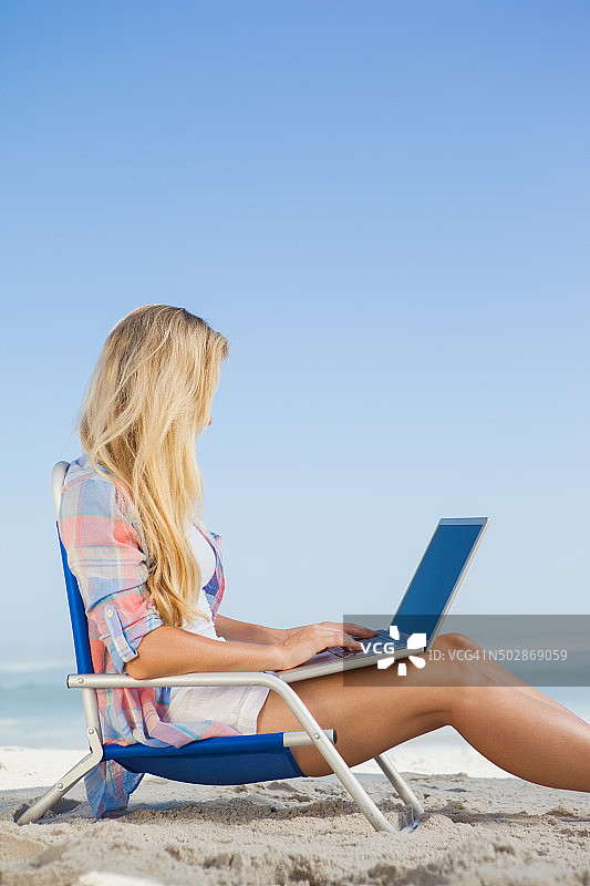 金发美女坐在沙滩上用笔记本电脑图片素材