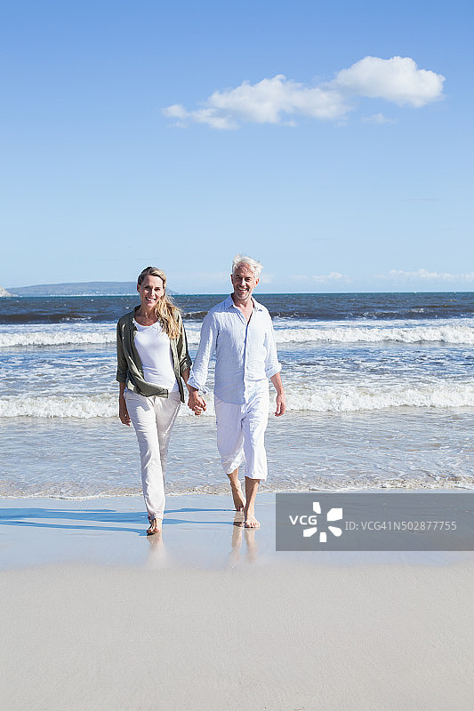 一对快乐的情侣光着脚在海滩上散步图片素材