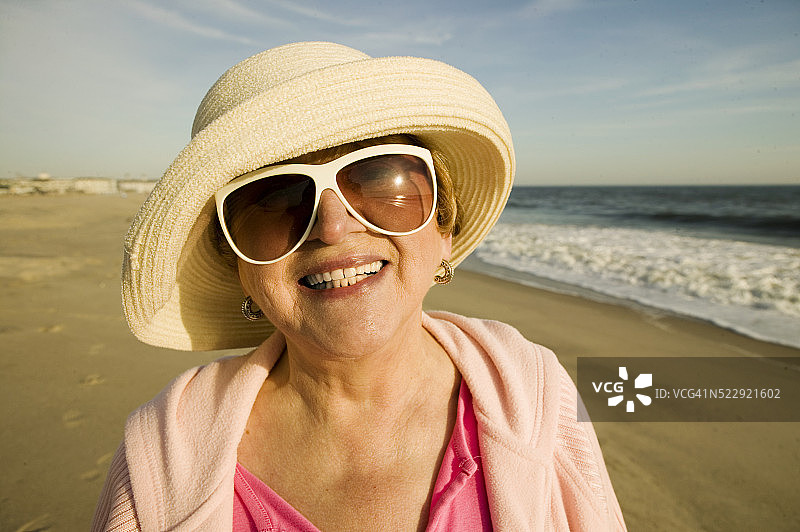 戴着帽子和太阳镜的老妇人在海滩上图片素材