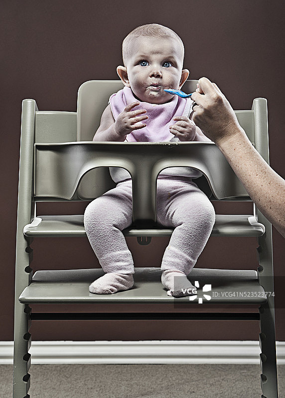 母亲喂养女婴(1-6个月)坐在高椅子上图片素材