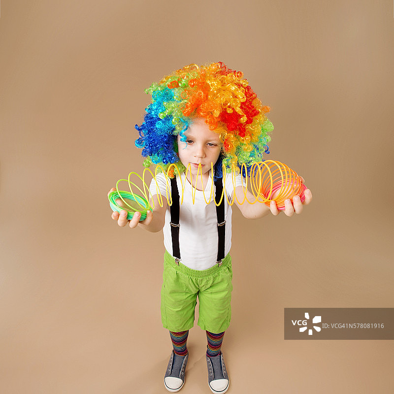 戴小丑假发的小男孩在玩弹簧。图片素材