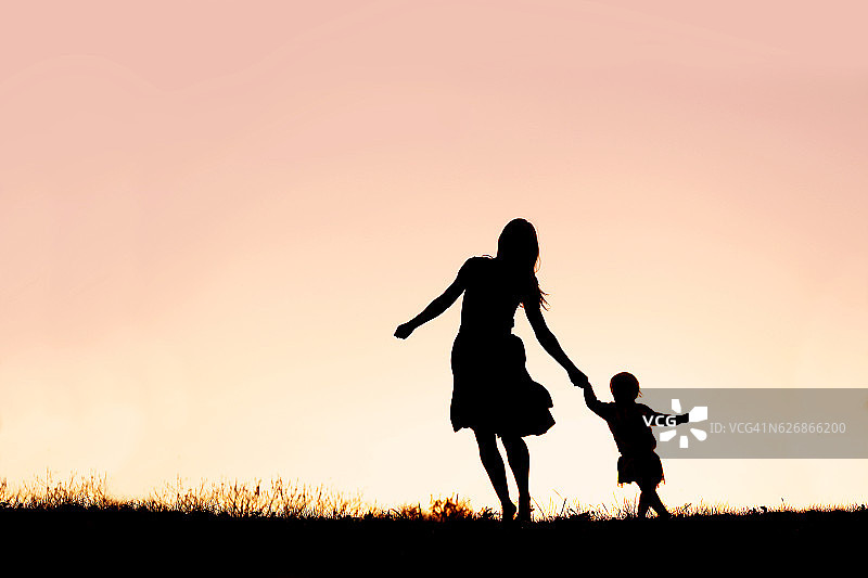 母亲和婴儿女儿在夕阳下奔跑和跳舞的剪影图片素材