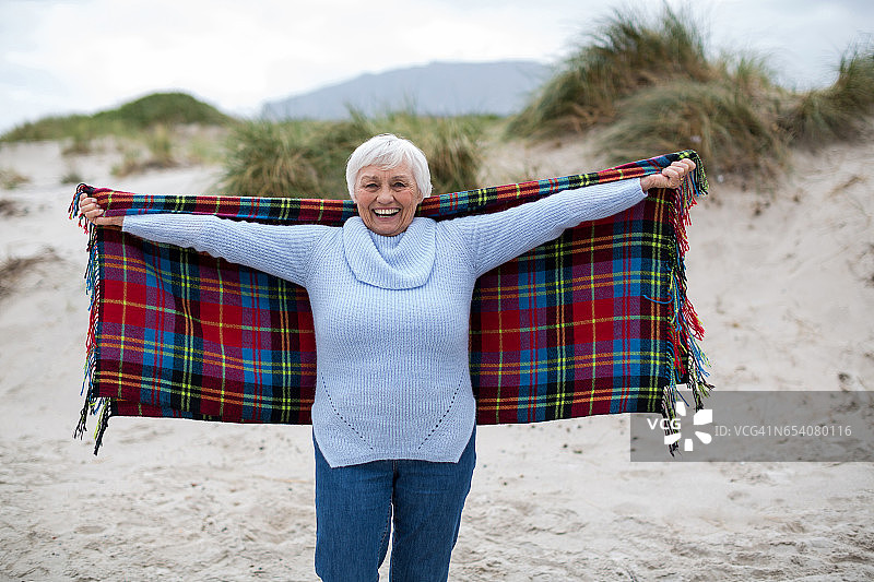 年长的女人张开双臂站在沙滩上图片素材