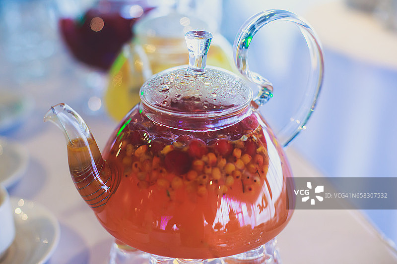 美丽温暖的图片透明茶壶茶壶与可口的红茶与苹果，柠檬和姜在桌子上蜡烛和甜点的背景图片素材