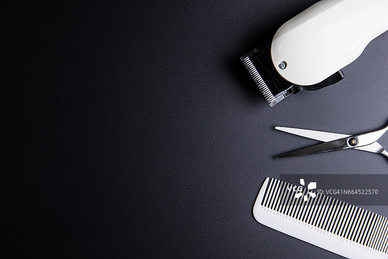时尚的专业理发剪刀，白色梳子和白色电动剪刀在黑色的背景。美发沙龙概念，美发套装。剪头发配件。复制空间图像，平铺。图片素材
